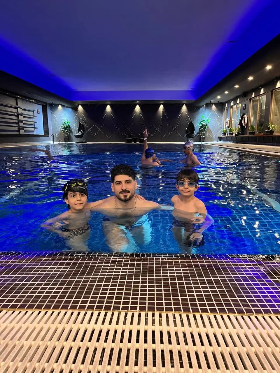 مربی و دو کودک آرام در آب تا سینه کنار لبهٔ استخر؛ غلبه بر ترس از آب